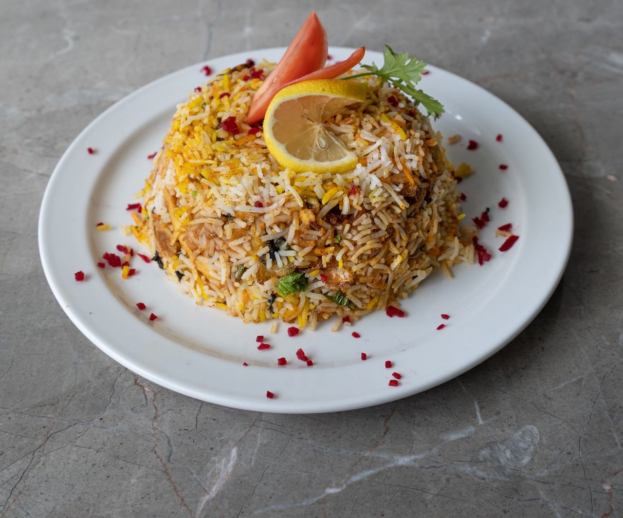 A vibrant plate of biryani garnished with lemon and tomatoes on a marble surface.